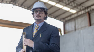 Civil engineer or manager with suit and safety hat stands confident in his precast factory. Factory owner in formal dress look forward for his success in a factory